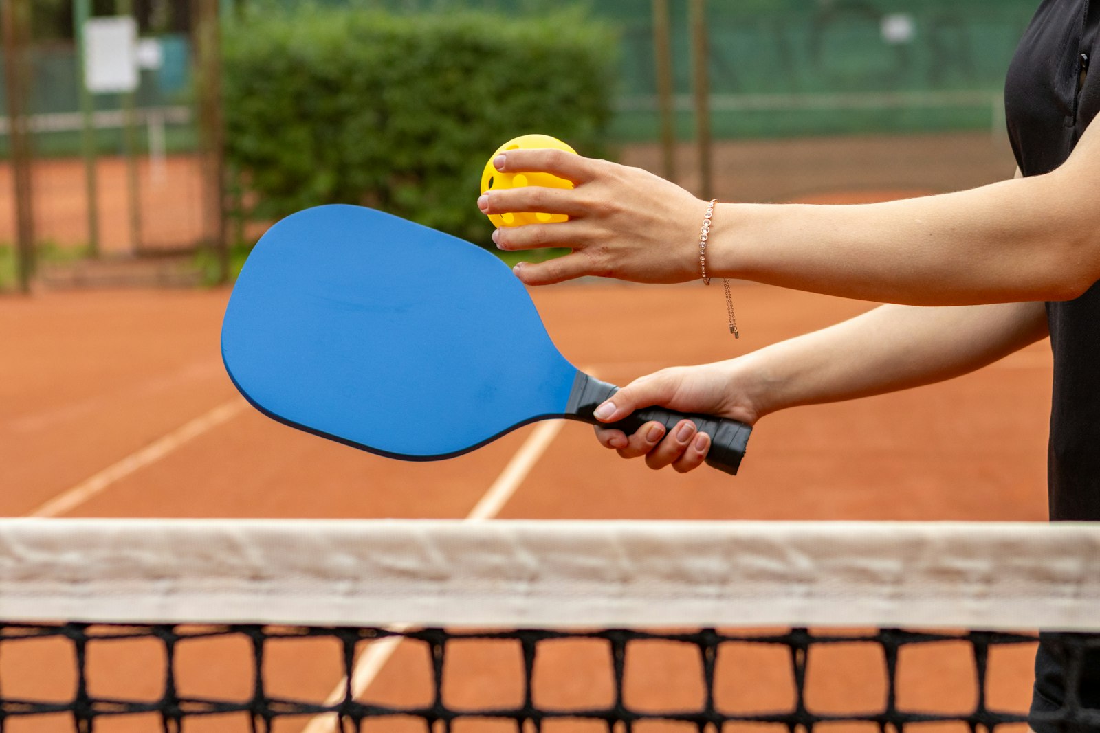 A player holding a paddle and ball at the net